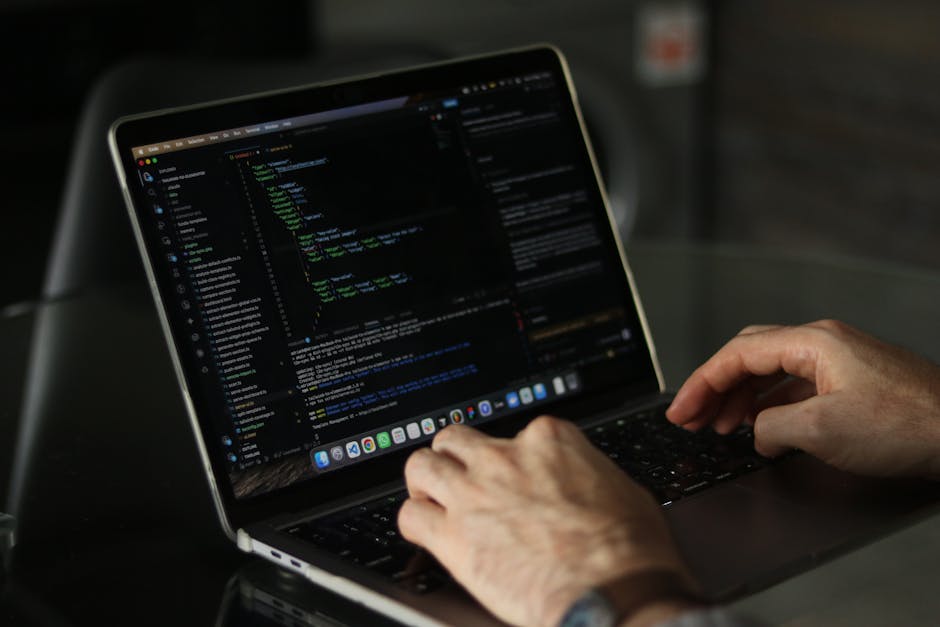 A close-up view of a laptop displaying lines of green, blue, and white code on a dark background, positioned on a wooden desk. Next to the laptop, there is a ceramic coffee mug with a cream-colored fi
